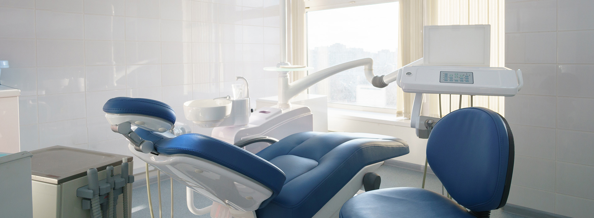 The image shows a modern dental clinic interior with various pieces of equipment, including a dental chair and an X-ray machine.
